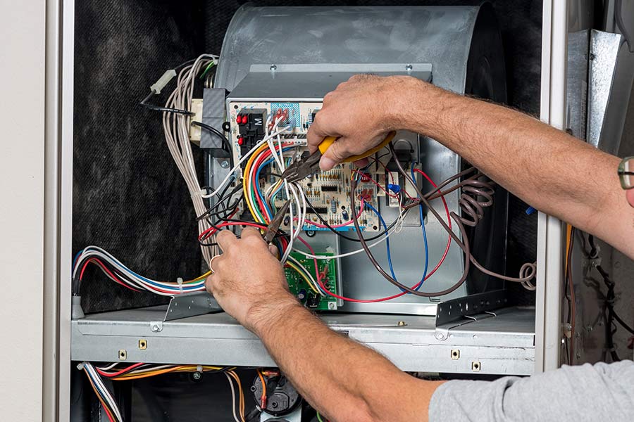 Technician repairing HVAC wiring inside a furnace unit